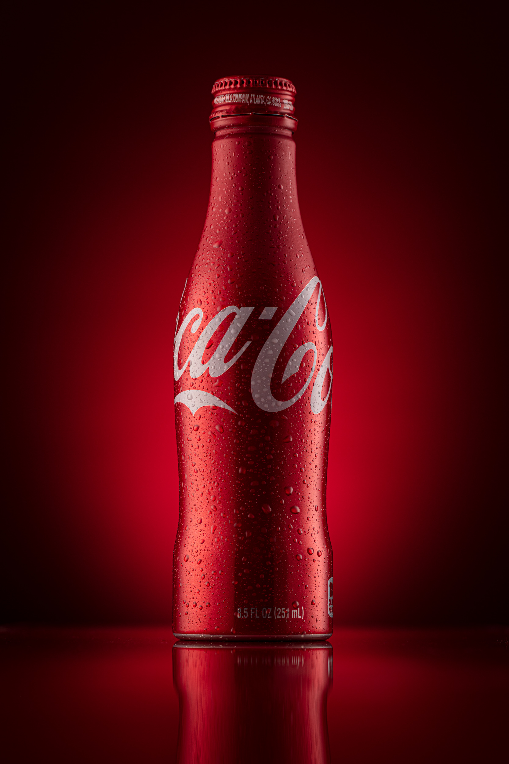 Still life product photo of a Coke bottle with condensation against a red backdrop in studio in Boulder, Colorado..