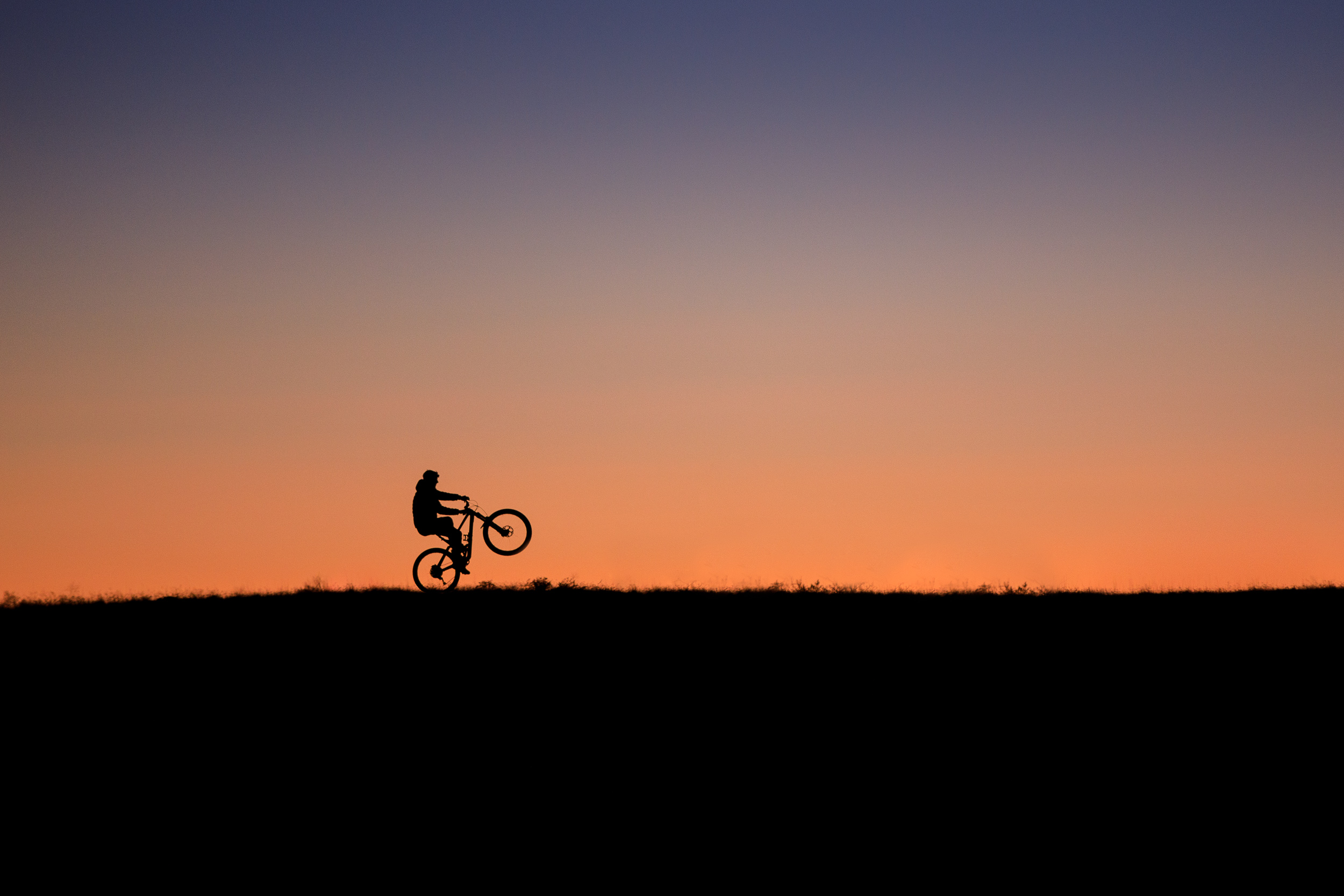 Mountain biker doing a wheelie silhouetted against the sunset in Fruita Colorado.