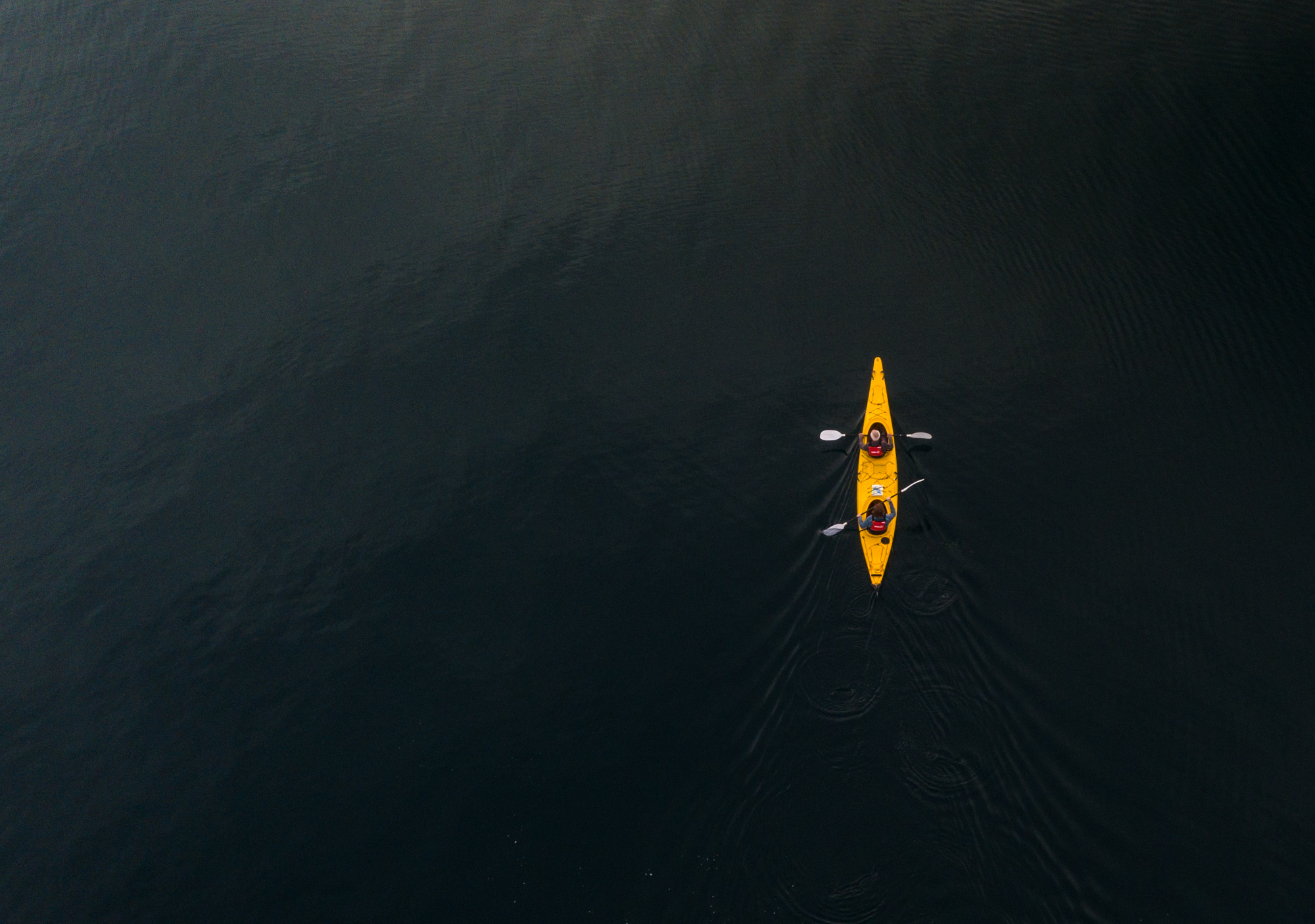 Lifestyle aerial drone photo of two people kayaking in yellow kayak in Wanaka, New Zealand.