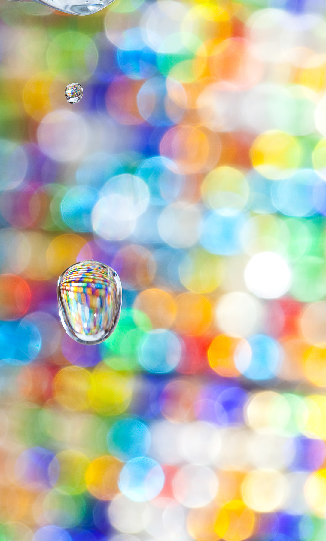 Macro Fine Art photo of a single water drop in the air refracting colored beads in the background.