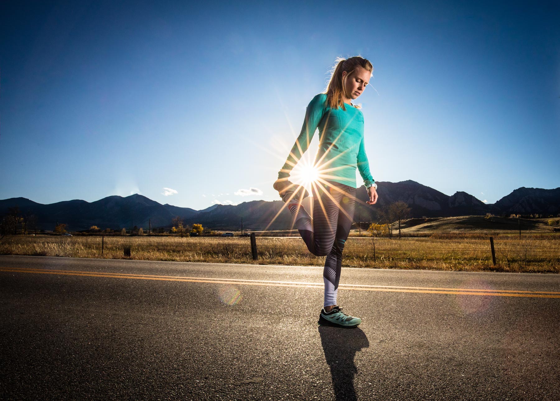 Active lifestyle photo of runner girl stretching on the road in Boulder, Colorado with sun streaming through.