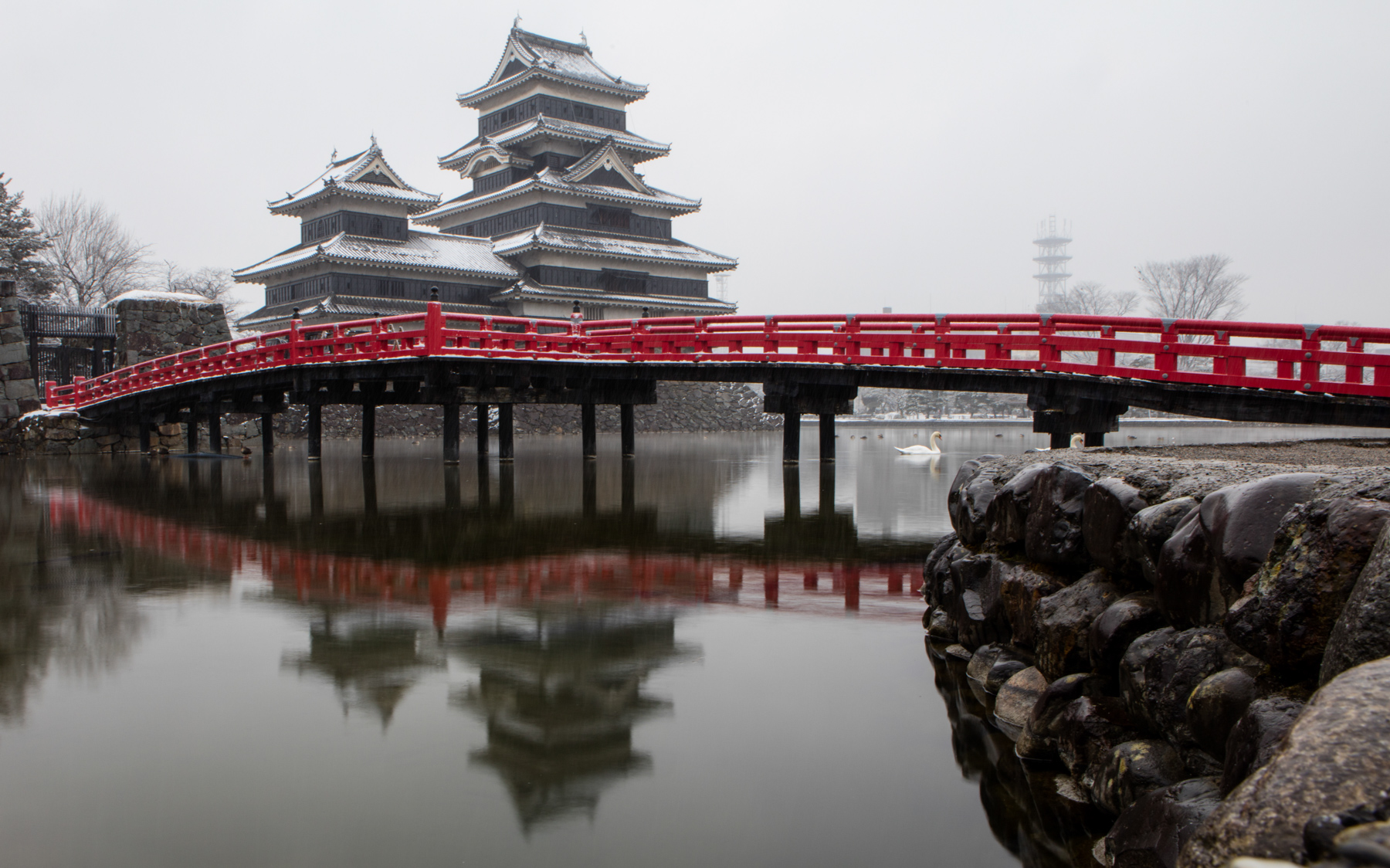 Matsumoto castle covered with snow and red bridge in front reflected in moat in Japan.