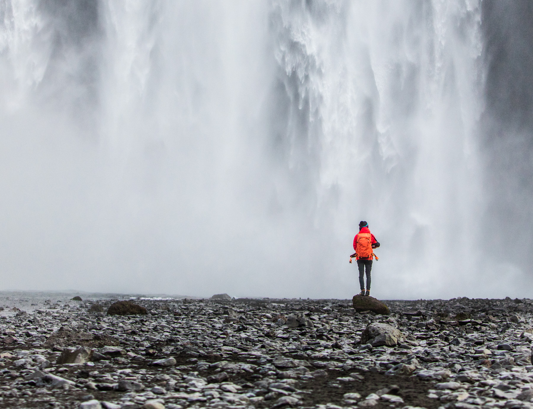 Active lifestyle photo of girl with red arcteryx jacket standing in front of a large waterfall in Iceland.